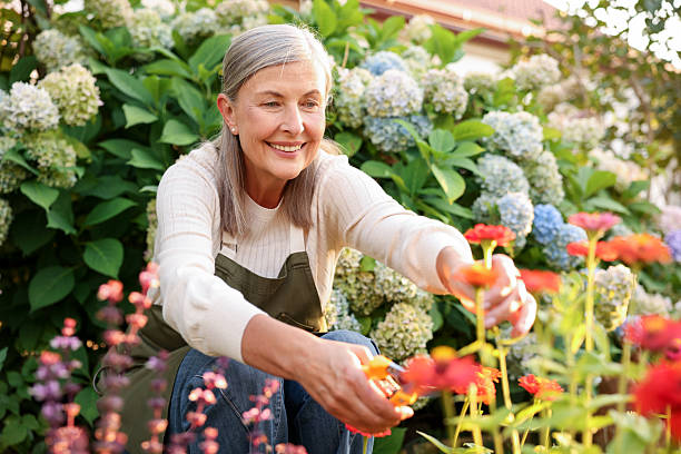 A smiling woman tending colorful flowers in her garden